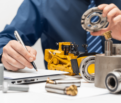 A man repairs a hydraulic pump while working on a laptop and taking notes with a pen.